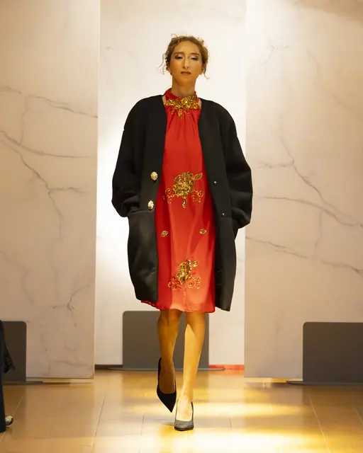 Robe Vermillon Dame en Soi — robe droite rouge brodée de motifs dorés portée sous un manteau noir oversize, défilé Galeries Lafayette